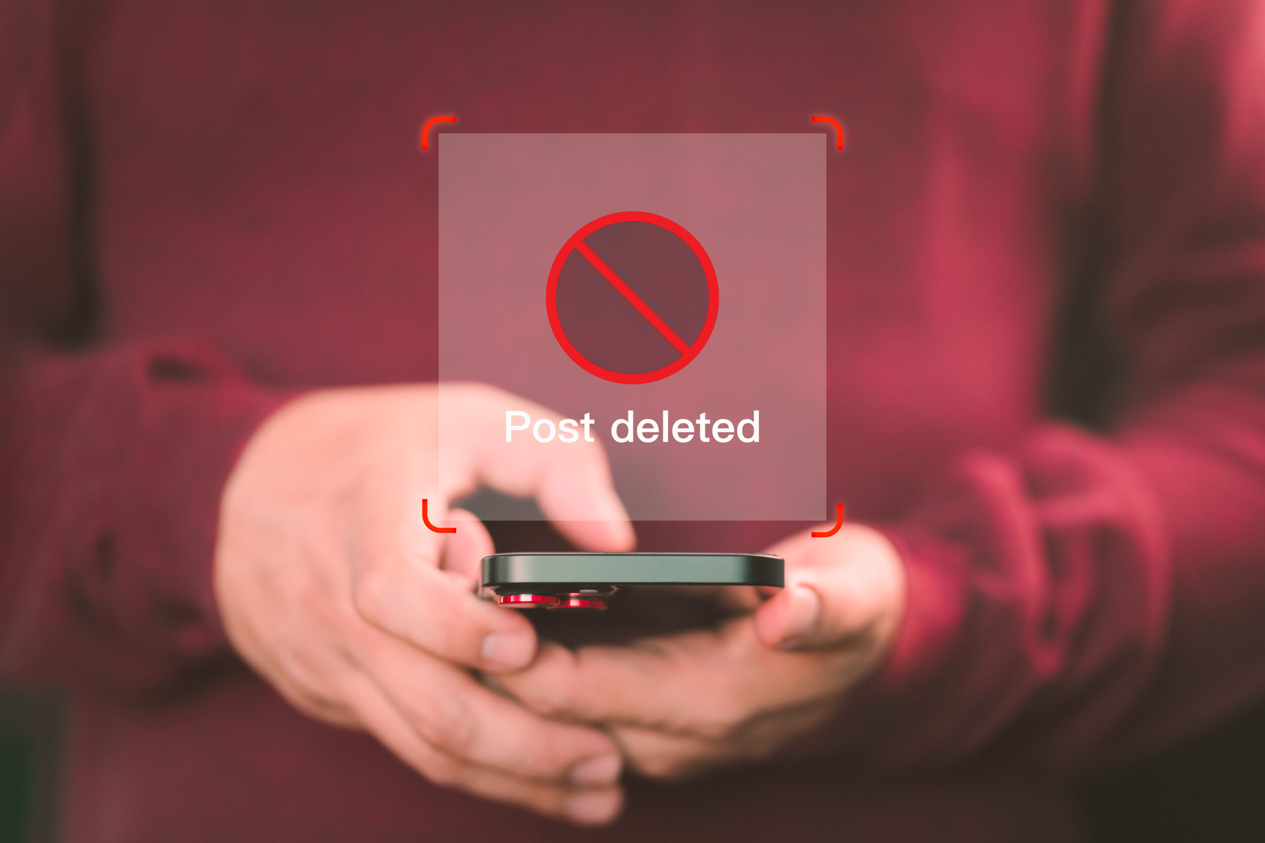 Person in a red sweater holding a phone that shows a deleted post